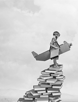 Enfant dans un avion en carton sur une pile de livres